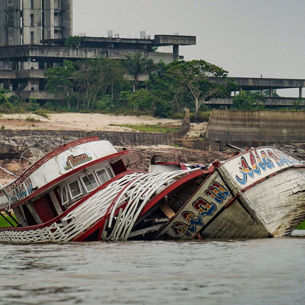 Foto mostra dois barcos encalhados em um rio. Ao fundo, um edifício rodeado de árvores